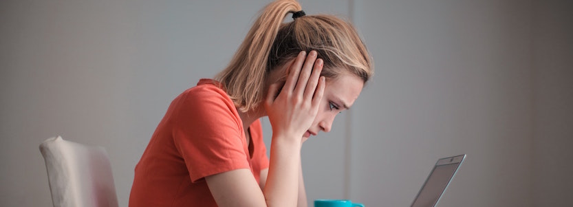 Young woman holding head in hands looking at computer